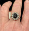 Ring with a dark blue sapphire gemstone and diamond accents on a finger against a dark background