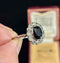 French Art Deco ring with a blue sapphire gemstone, made in platinum and held by a hand against a dark background