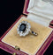 Vintage ring with a dark navy blue sapphire and diamond accents in an open jewelry box.