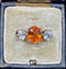 antique three-stone ring featuring a vibrant spessartite garnet center flanked by two round diamonds, set in 18ct yellow gold.