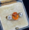 Rare spessartite garnet and diamond ring, highlighting a bright orange center stone surrounded by two clear diamonds in an elegant antique setting from 1915.