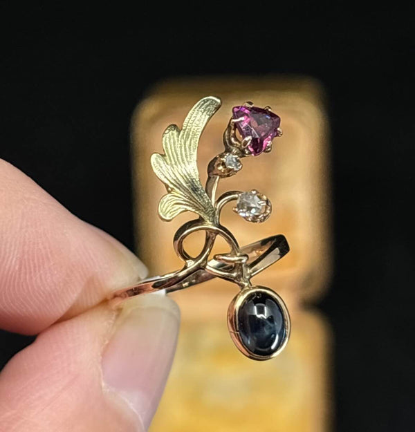 14ct rose and yellow gold Art Nouveau ring featuring a cabochon sapphire, 5mm garnet and two rose-cut diamonds.