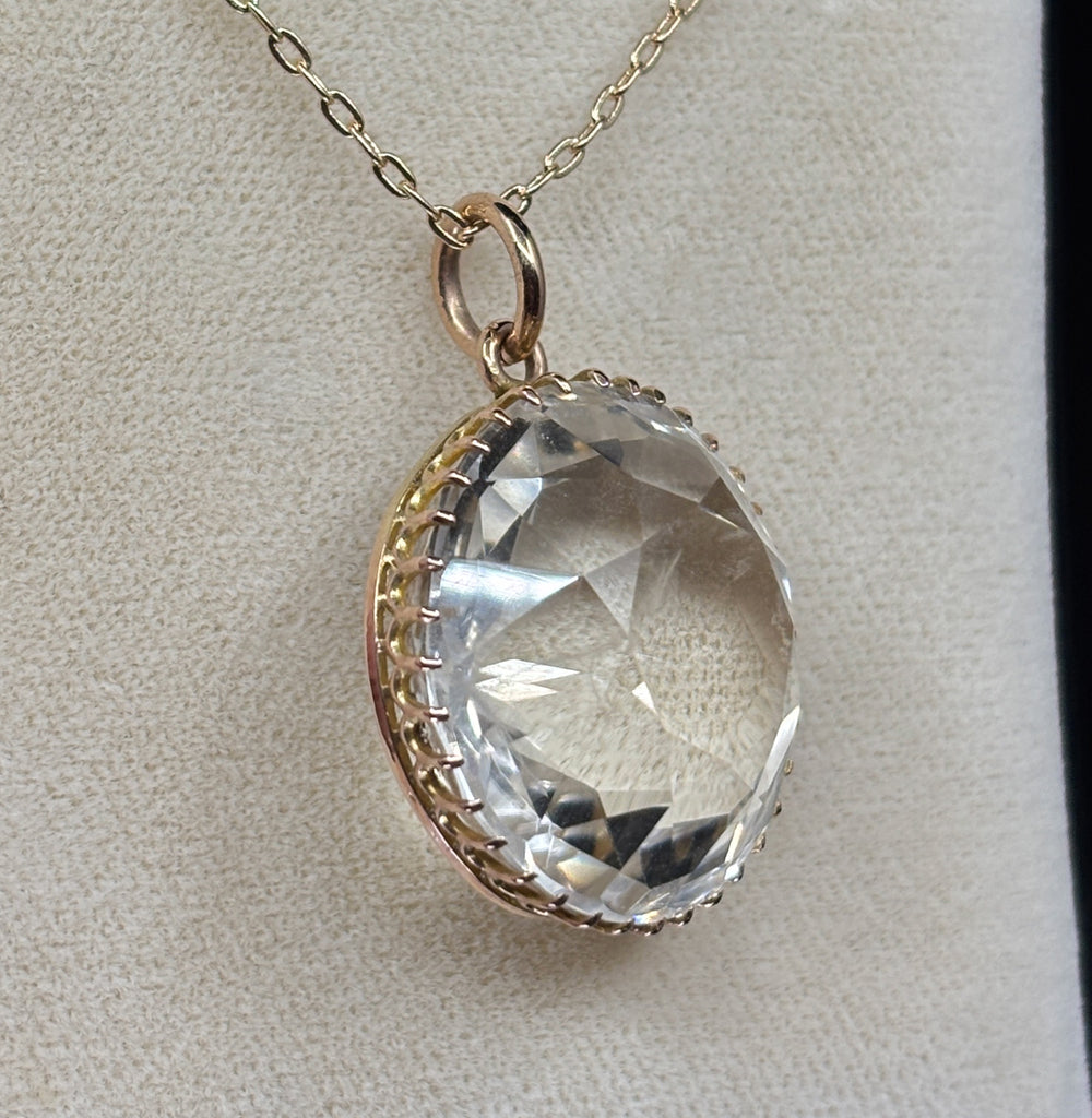 Angled view of the Victorian rock crystal pendant showing its high-domed faceted crystal and closed gold collet setting