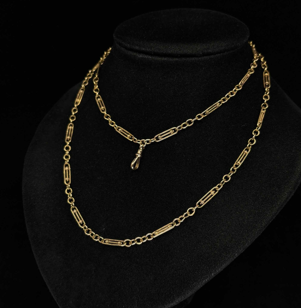 Antique Edwardian 9ct gold guard chain displayed long and doubled on a black stand, showing its original swivel clip