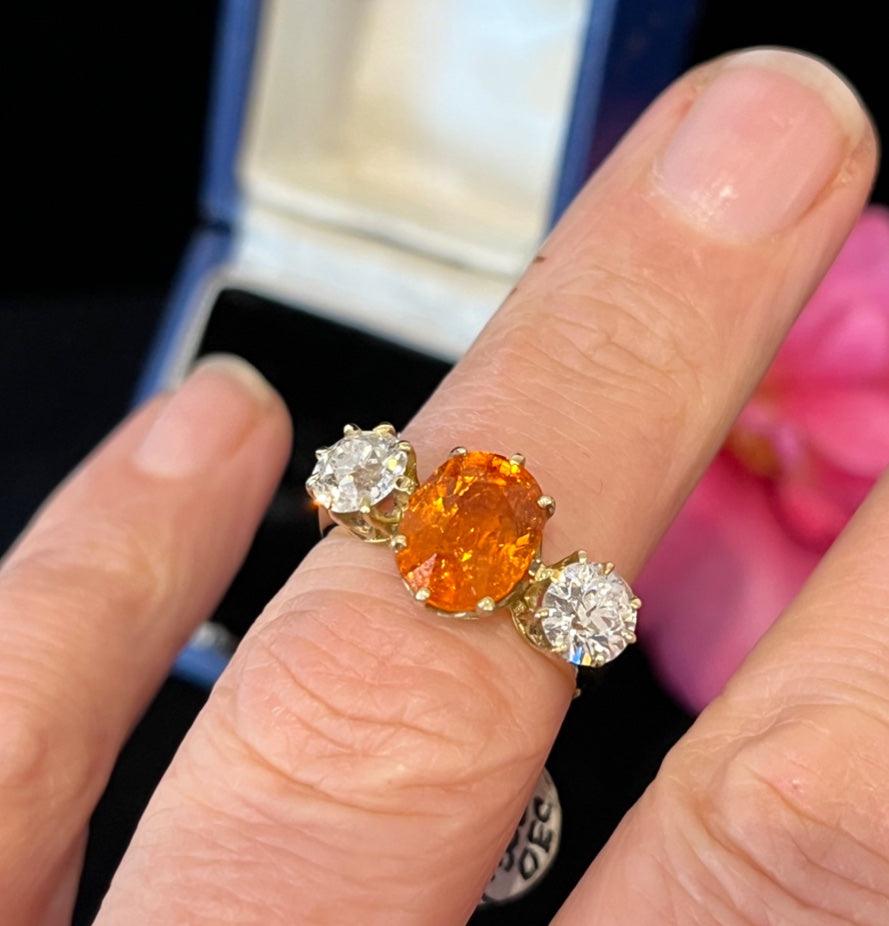 Spessartite garnet and old european cut diamond trilogy ring shown being worn on the finger.
