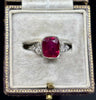1920s antique lady’s ruby ring with 2.83ct natural untreated cushion ruby in bezel, set in 18ct white gold and platinum with diamond‑set ornate shoulders.