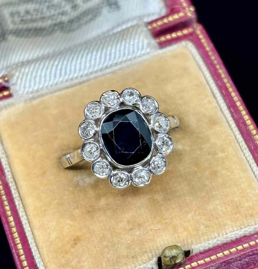 Antique ring with a dark bue sapphire gemstone and diamond accents on a velvet cushion