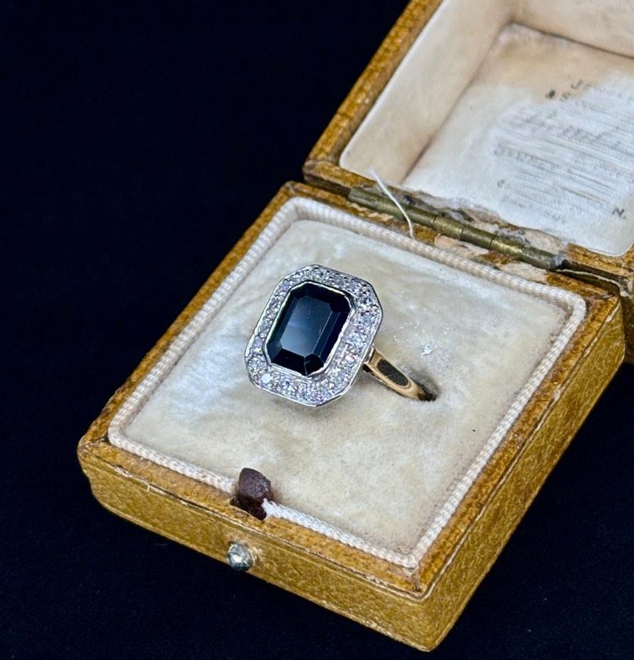 Antique 1930s emerald cut sapphire cluster ring featuring a bezel-set sapphire surrounded by diamonds.