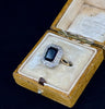 Antique 1930s emerald cut sapphire cluster ring featuring a bezel-set sapphire surrounded by diamonds.