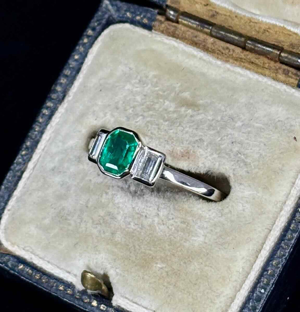 A bezel set antique 1940s emerald and diamond ring featured in an antique ring box.