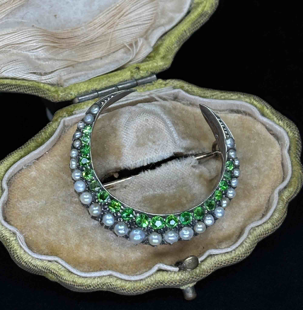 Angled view of the Victorian crescent moon brooch with graduated demantoid garnets and natural pearls in its antique case