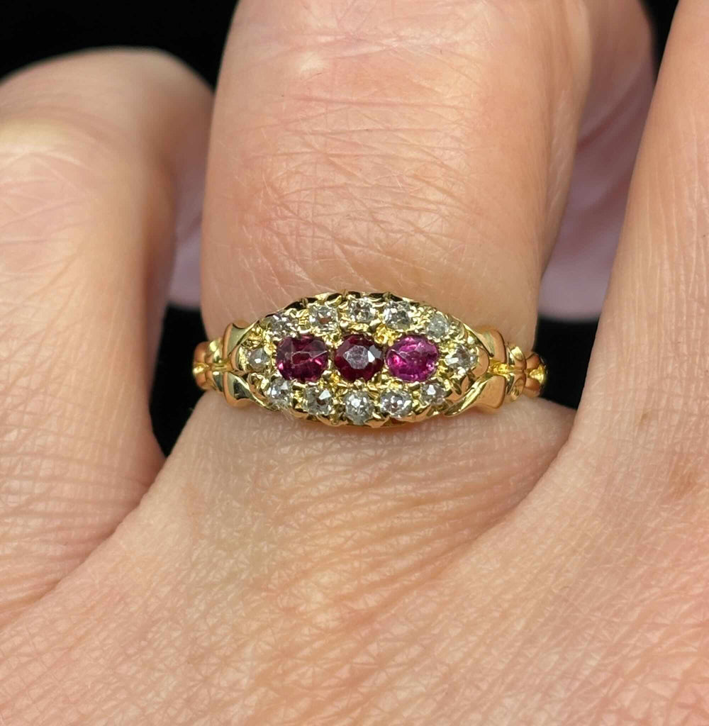 Antique Edwardian ruby and diamond cluster ring worn on the hand, showing three round rubies and old mine cut diamond halo