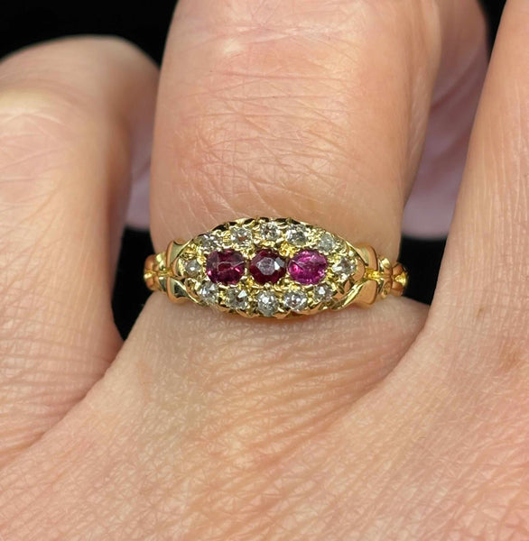Antique Edwardian ruby and diamond cluster ring worn on the hand, showing three round rubies and old mine cut diamond halo