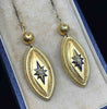 Angled close-up of antique Victorian gold earrings showing enamel starbursts, seed pearls and intricate cannetille borders