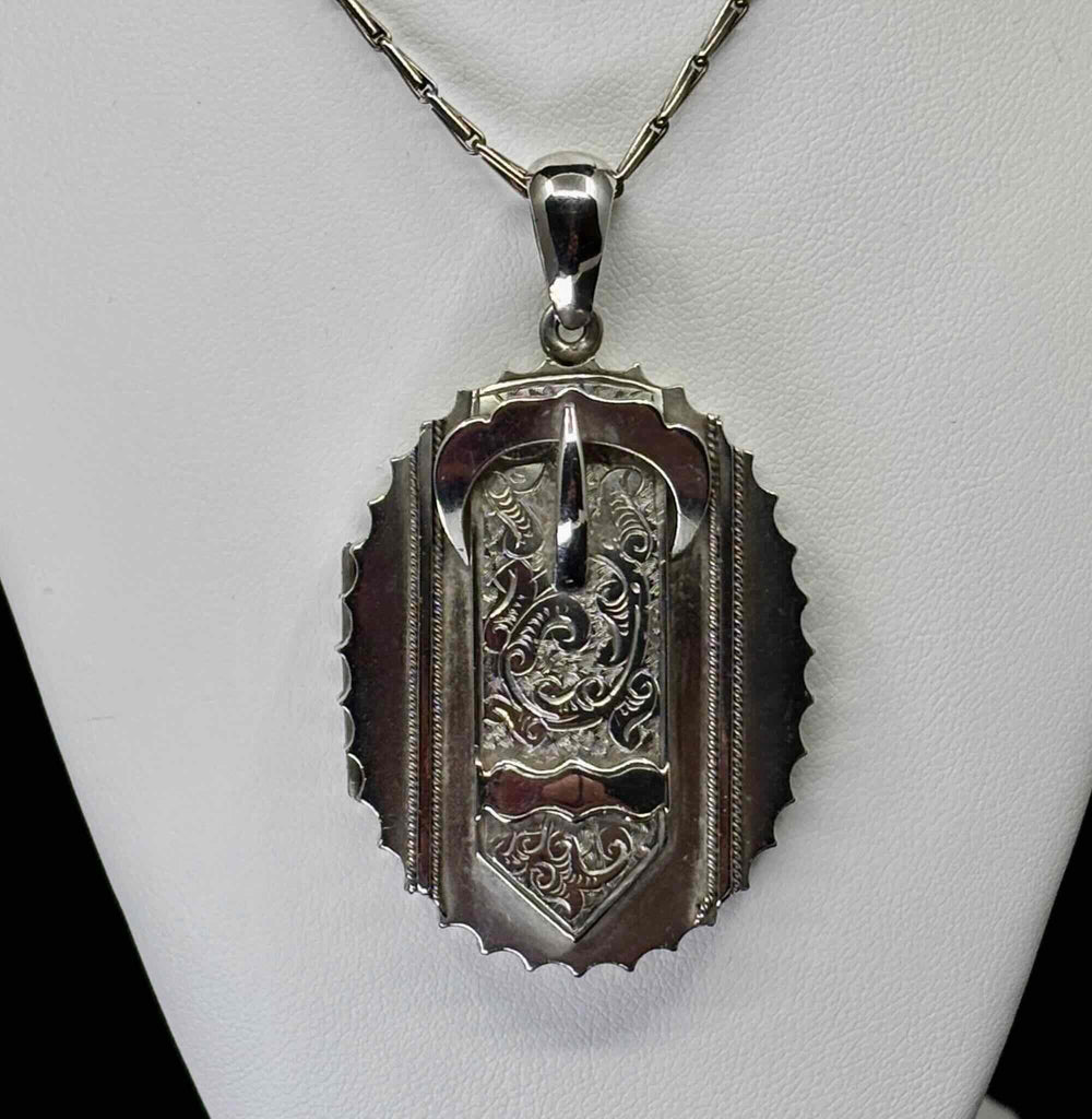 Front view of an antique Victorian sterling silver buckle locket with hand-engraved foliate scrollwork and scalloped border