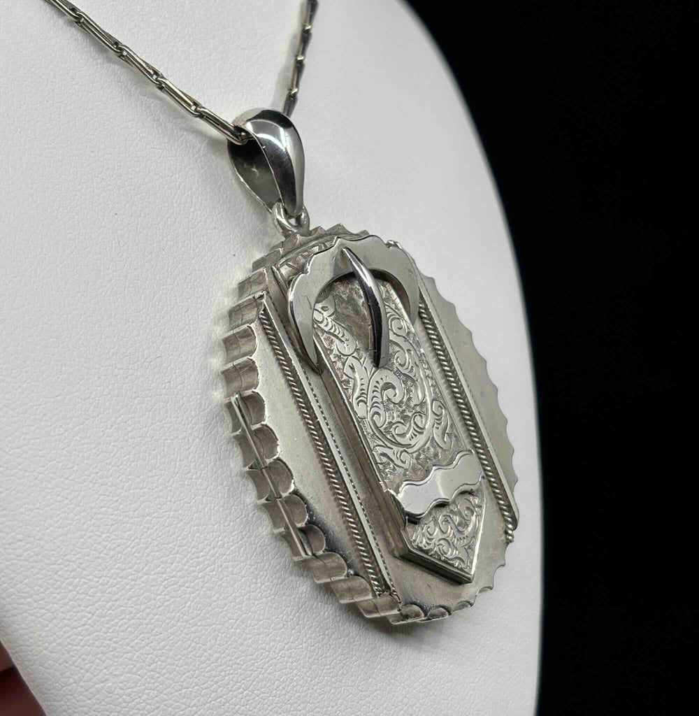 Angled view of the antique Victorian silver buckle locket showing its engraved belt buckle motif and saw-cut scalloped edge