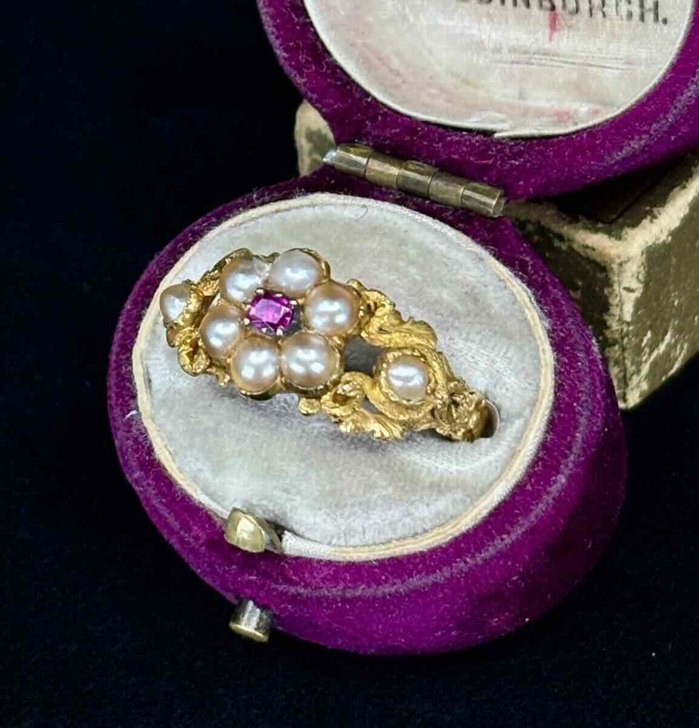 Gold ring with pearls and a ruby and pearl gemstones in an antique, open purple ring box.