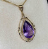 Up close detail of delicate yellow gold frame and pear shaped purple amethyst against a cream background