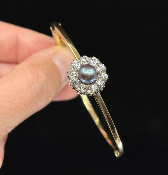 Close-up of an antique hinged bangle featuring a natural black pearl surrounded by diamonds, held in hand.