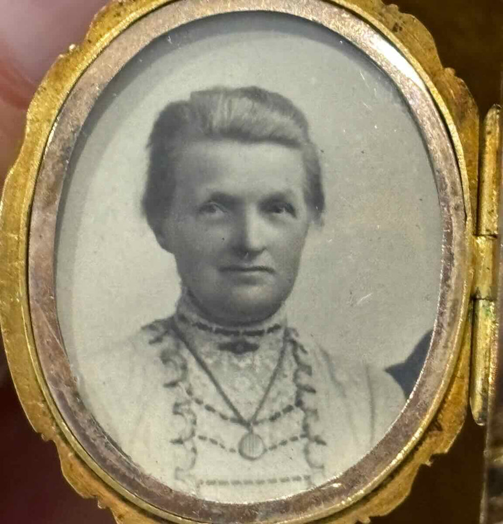 Close up of the woman's portrait inside the antique Victorian gold locket. Pictured she is wearing the locket on a long chain with a brooch directly above sitting on her collar.