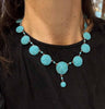 Antique Victorian turquoise necklace set in gold photographed on the neckline vividly contrasting aqua blue against a black top.