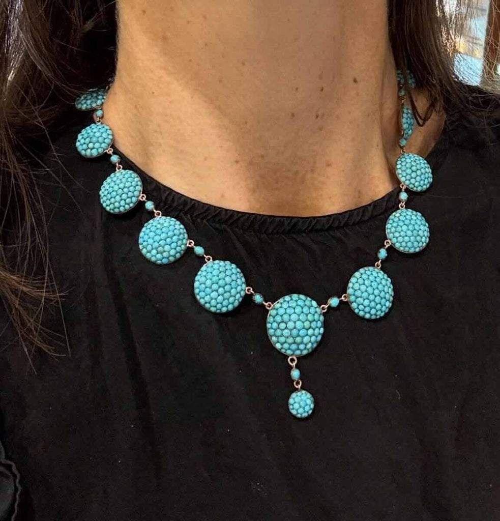 Antique Victorian turquoise necklace set in gold photographed on the neckline vividly contrasting aqua blue against a black top.