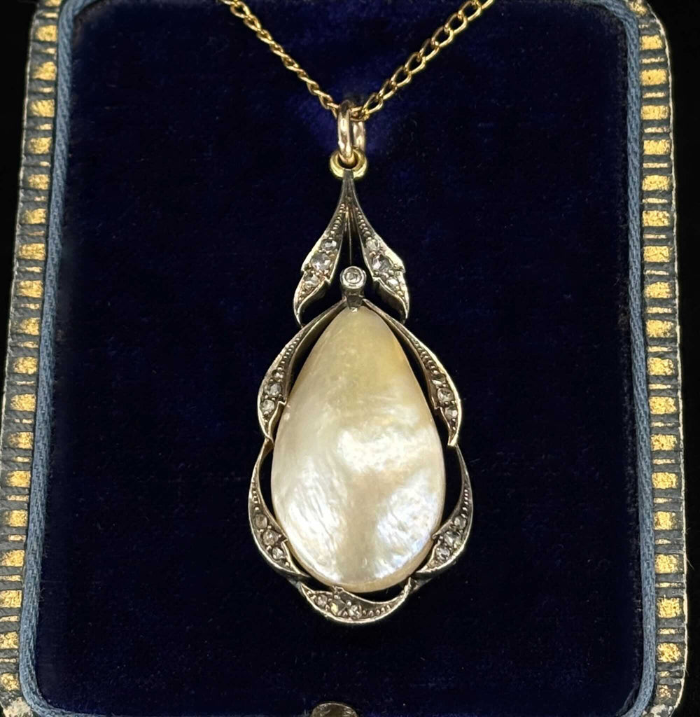 An antique pear shaped pearl pendant in silver and gold setting with rose cut diamonds, displayed on a dark blue antique velvet jewellery box.