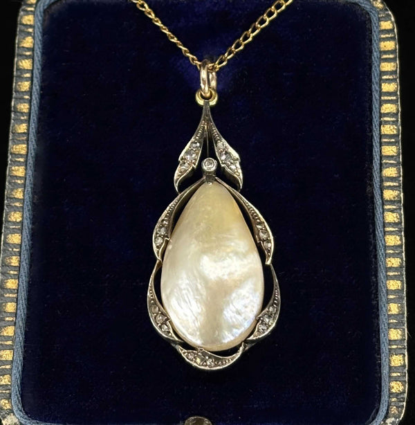 An antique pear shaped pearl pendant in silver and gold setting with rose cut diamonds, displayed on a dark blue antique velvet jewellery box.