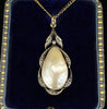 An antique pear shaped pearl pendant in silver and gold setting with rose cut diamonds, displayed on a dark blue antique velvet jewellery box.
