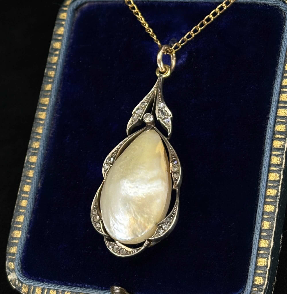 Side view of an antique pear shaped pearl pendant in silver and gold setting with rose cut diamonds, displayed on a dark blue antique velvet jewellery box.