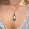 A close-up of a women's neck and chest wearing a gold chain necklace with a teardrop-shaped cream pearl pendant in a silver and 18ct yellow gold setting.