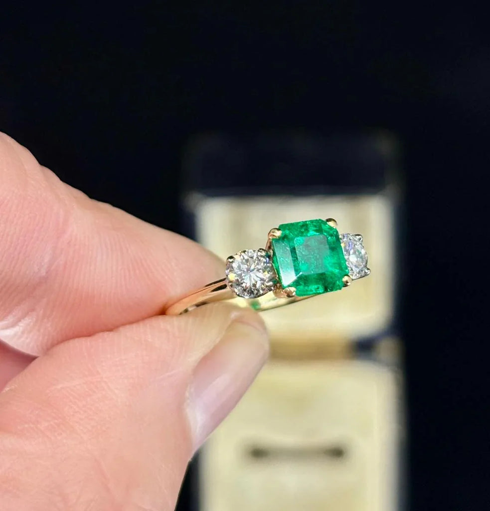 Classic 1950s emerald ring featuring diamond shoulder accents in a gold setting.