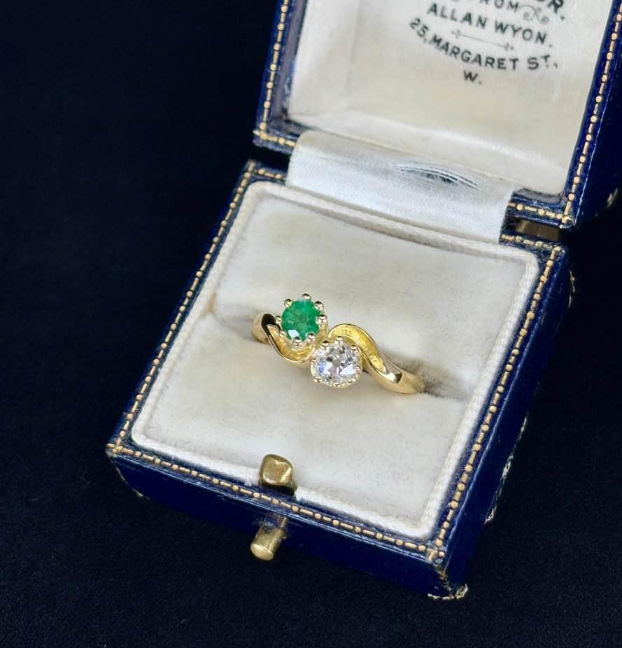 A stunning Edwardian-emerald-and-diamond-'Toi-et-Moi'-ring featuring a vibrant emerald and old cut diamond set in 18ct yellow gold.