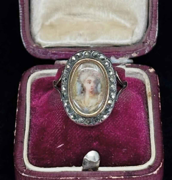 A elegant 19th century Georgian ring of a painted portrait of a young upper class lady behind rock crystal and a marcasite surround in an antique ring box