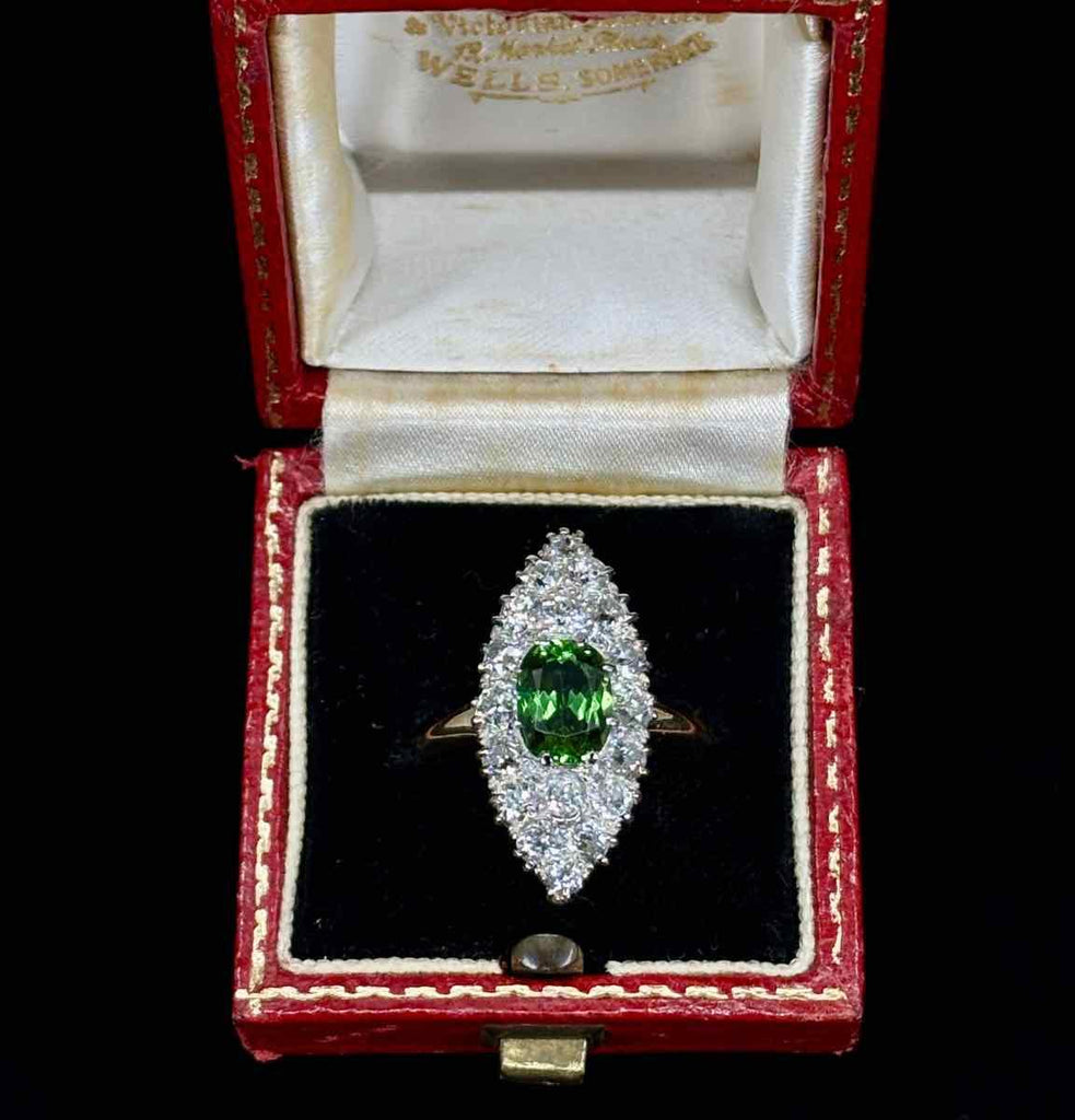 A hand holding a beautiful antique ring with a vibrant green peridot and sparkling diamonds, showcasing exquisite Victorian craftsmanship.