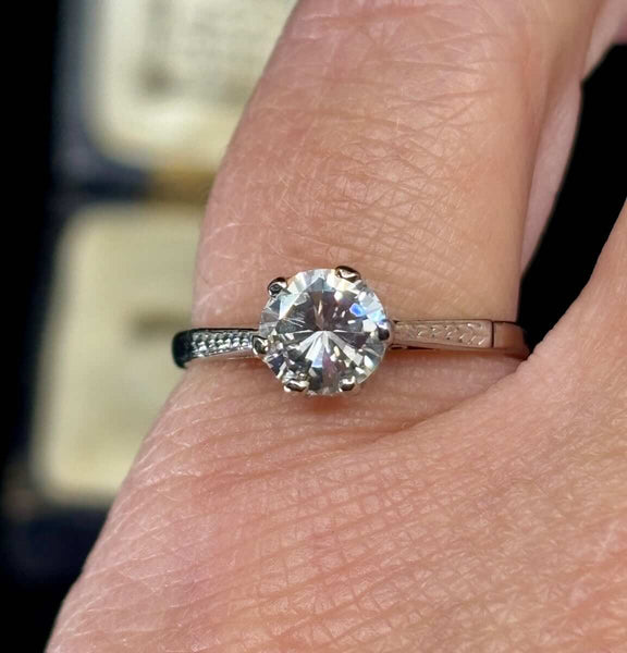 Platinum and diamond solitaire engagement ring on finger showing off the hand engraved feathering