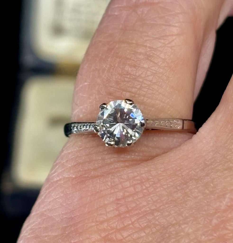 Platinum and diamond solitaire engagement ring on finger showing off the hand engraved feathering