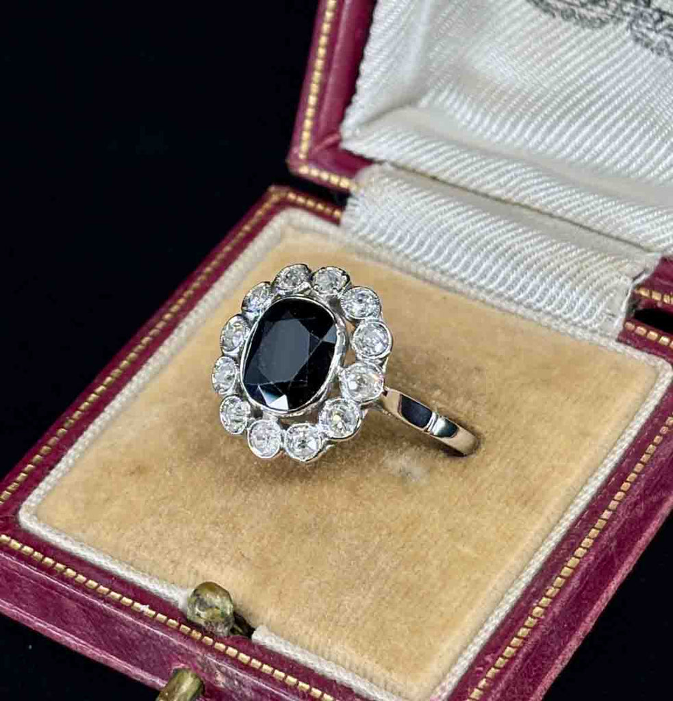 Vintage ring with a dark navy blue sapphire and diamond accents in an open jewelry box.