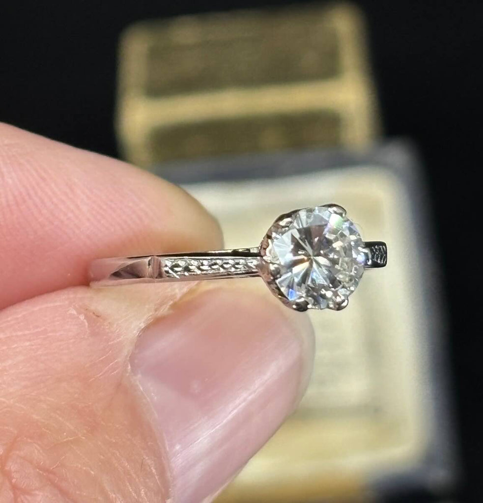 Round brilliant cut Diamond ring held between fingers showing off hand engraved platinum detailing on side