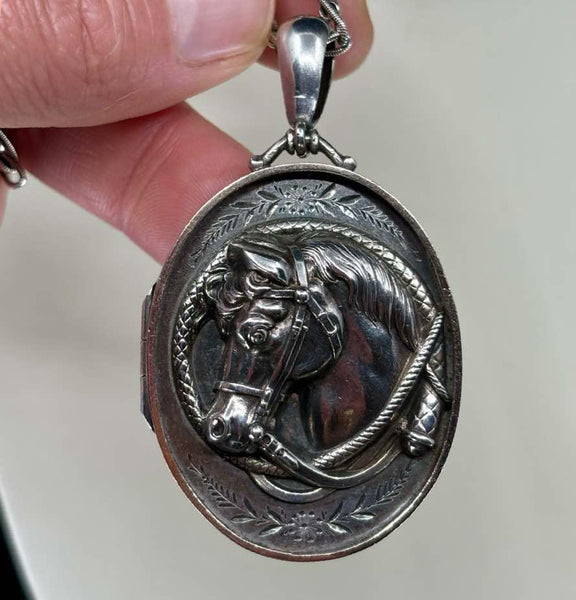 The front of a Victorian silver horse shoe locket with a horse's head surrounded by a riding crop in the shape of a horse shoe