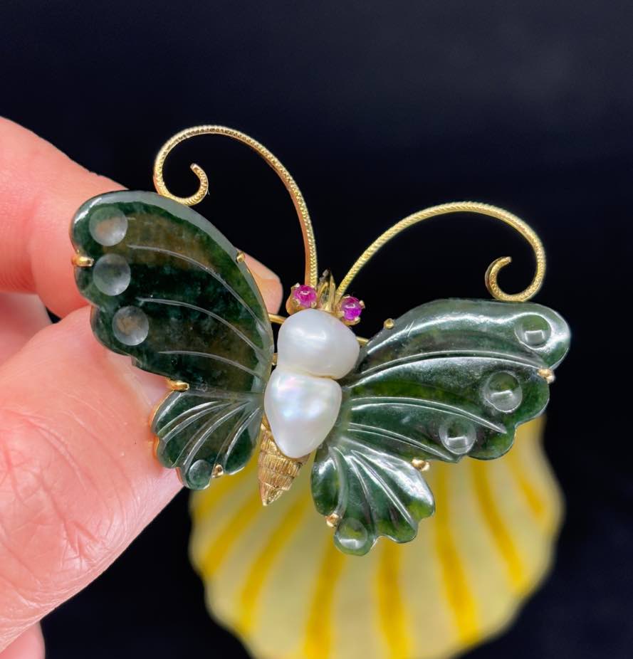 Close-up of a vintage butterfly brooch featuring a large baroque freshwater pearl, nephrite wings, and ruby eyes set in 14ct yellow gold.