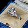 A round brilliant-cut diamond engagement ring with a white  and yellow gold band, displayed in a beige velvet ring box.