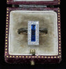 Front view of an antique Art Deco sapphire and diamond rectangular cluster ring held between fingers.
