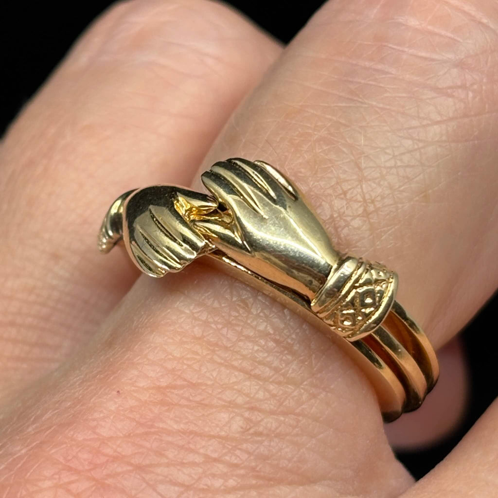 Close up of clasped hands motif on antique yellow gold fede ring.