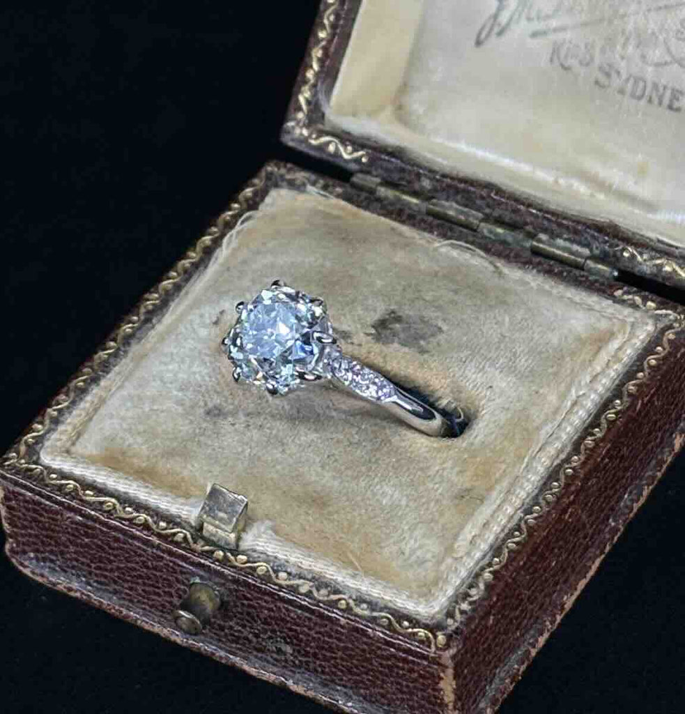 Antique diamond ring featuring a central old mine cut diamond and round brilliant cut diamonds on the shoulders.