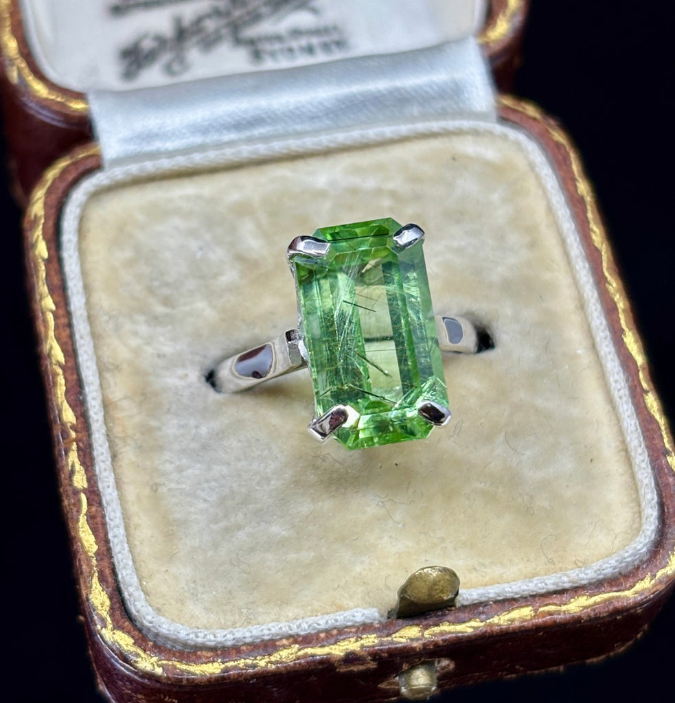 antique emerald cut green peridot ring photographed on a diagonal view showing the white gold band