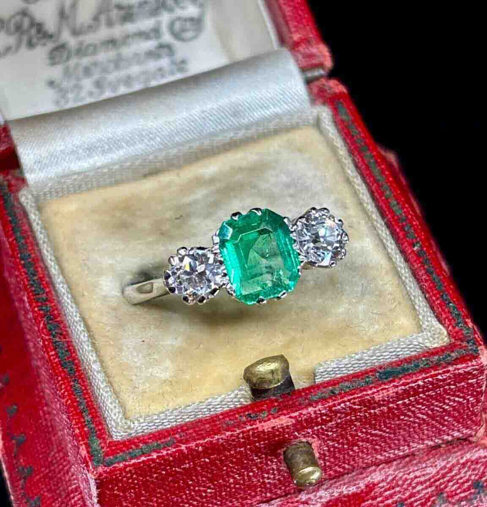 Antique three‑stone platinum ring featuring a natural Colombian emerald flanked by sparkling old European diamonds.