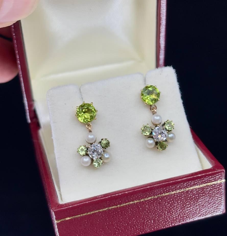 Close-up view of antique Edwardian earrings with old mine cut diamonds, vibrant peridots, and lustrous pearls, highlighting intricate craftsmanship and design.