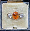 antique three-stone ring featuring a vibrant spessartite garnet center flanked by two round diamonds, set in 18ct yellow gold.