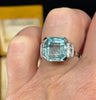 Four claw aquamarine and diamond ring featured on the finger.